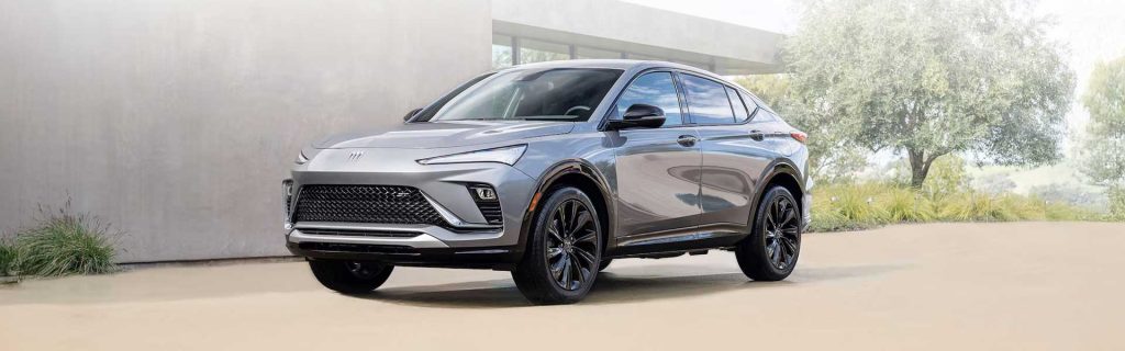 2025 Buick Envista in sleek silver parked in a modern driveway, showcasing its aerodynamic design, black alloy wheels, and stylish front grille.