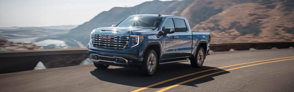 2025 GMC Sierra 1500 on a road, sunlight shinning on the windshield with mountains in the background.