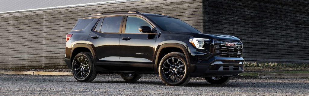 2025 GMC Terrain SUV in black parked near a modern wooden building, showcasing its bold exterior design and refined styling.