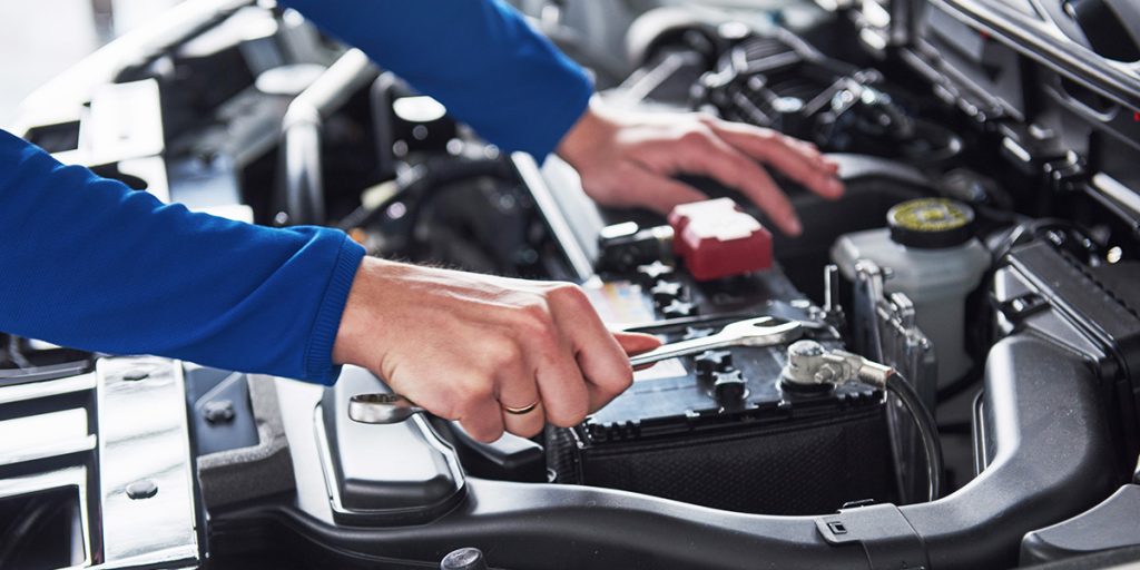 Close-up of a mechanic's hands using a wrench to work on a car battery.