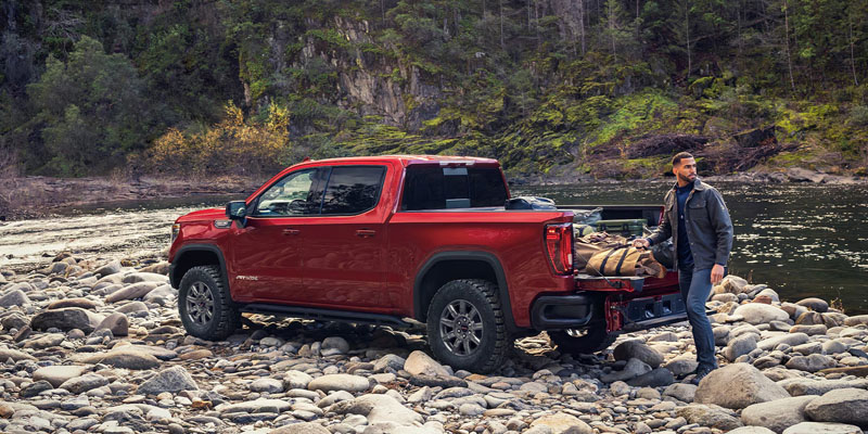 A red GMC Sierra pickup truck on a rocky riverbank.