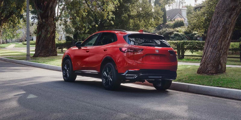 Red Buick Envision driving along a tree-lined residential street.